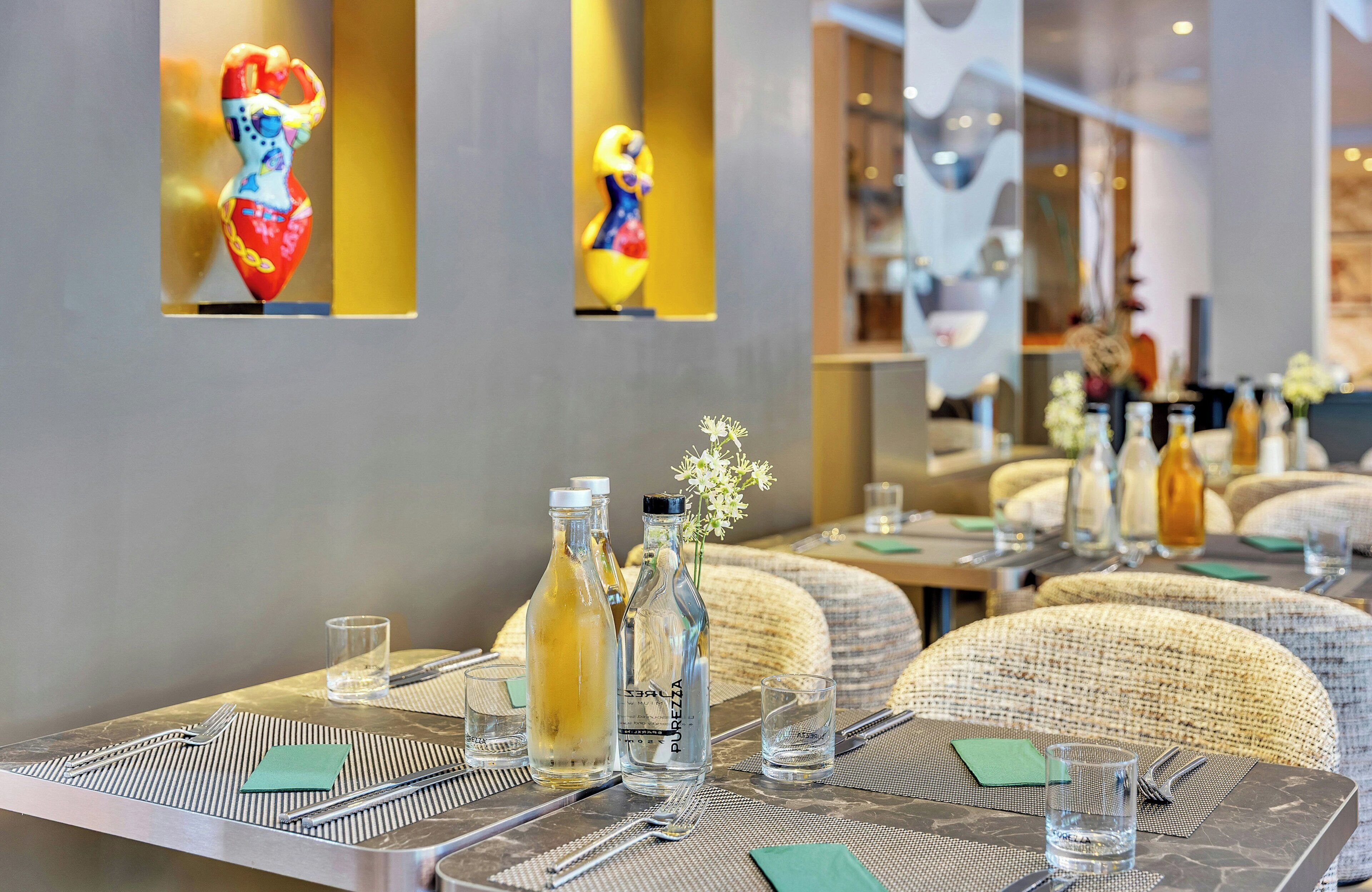 Ein Restaurantinneres mit gedeckten Tischen, Glasflaschen und einer Vase mit Blumen.