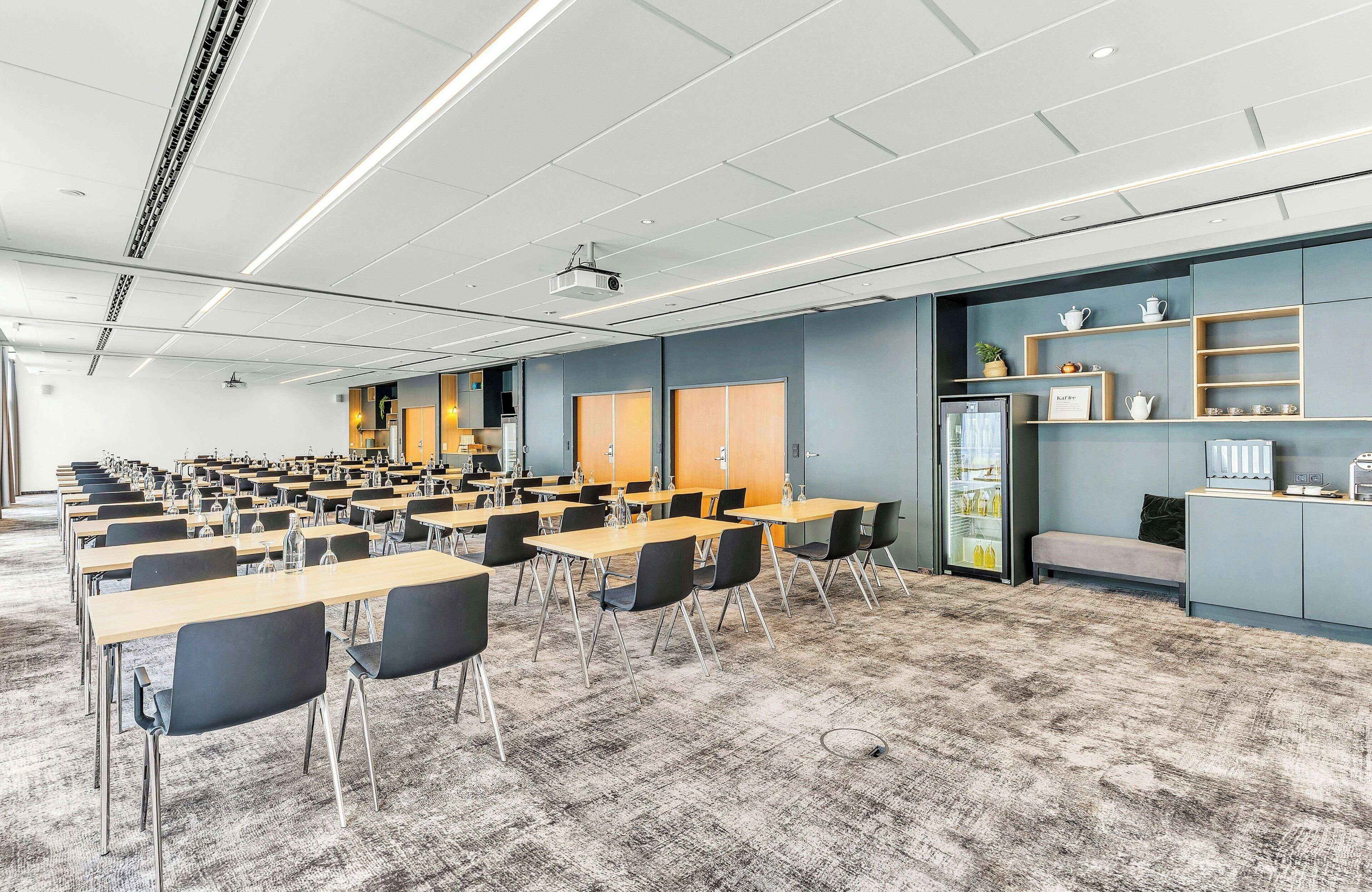 A conference room with rows of tables and chairs, a projector, and a refrigerator.
