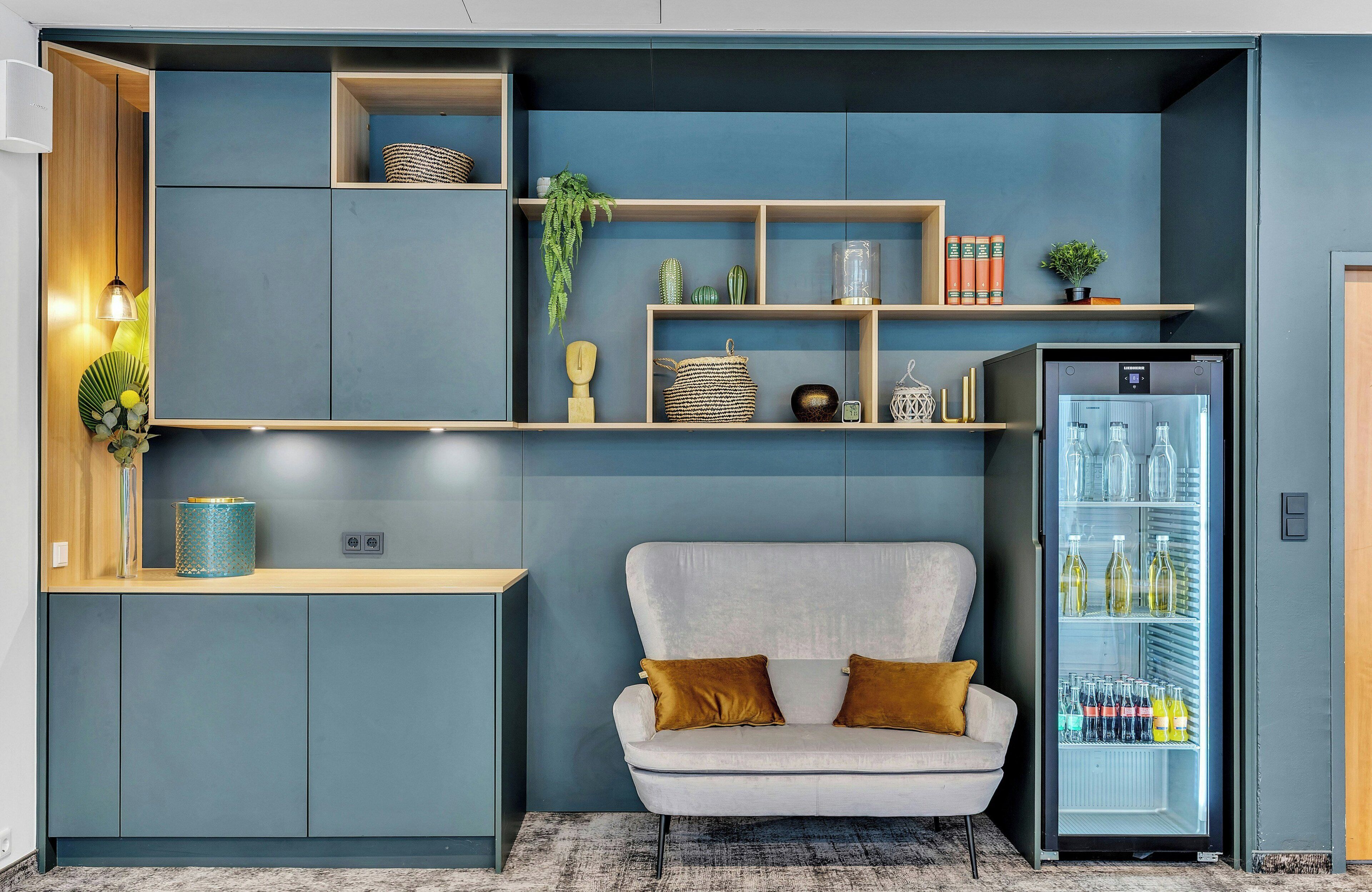 A modern kitchenette with a built-in fridge, a white sofa, and a wooden countertop.