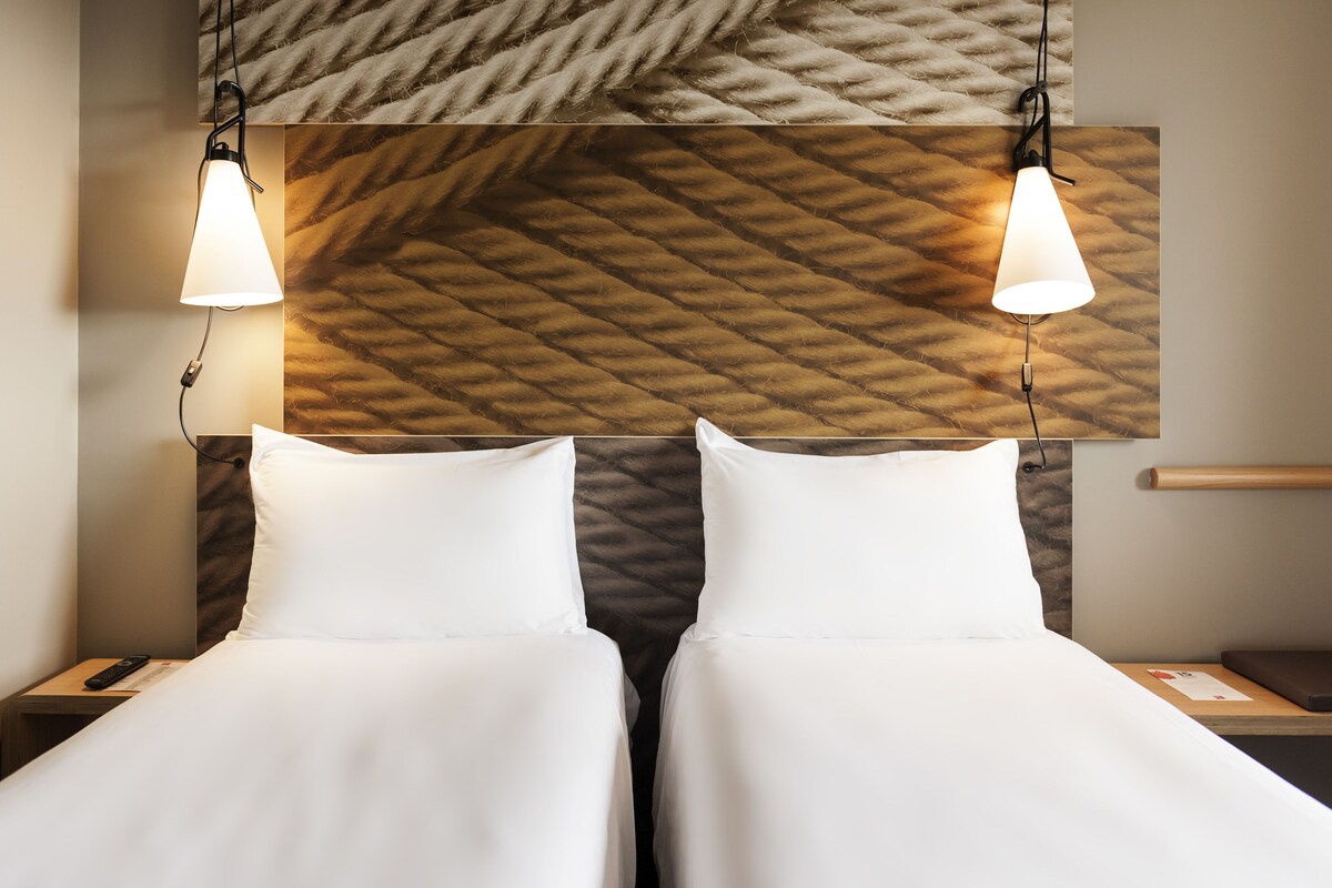 A hotel room with two beds, a wooden headboard, and pendant lighting.