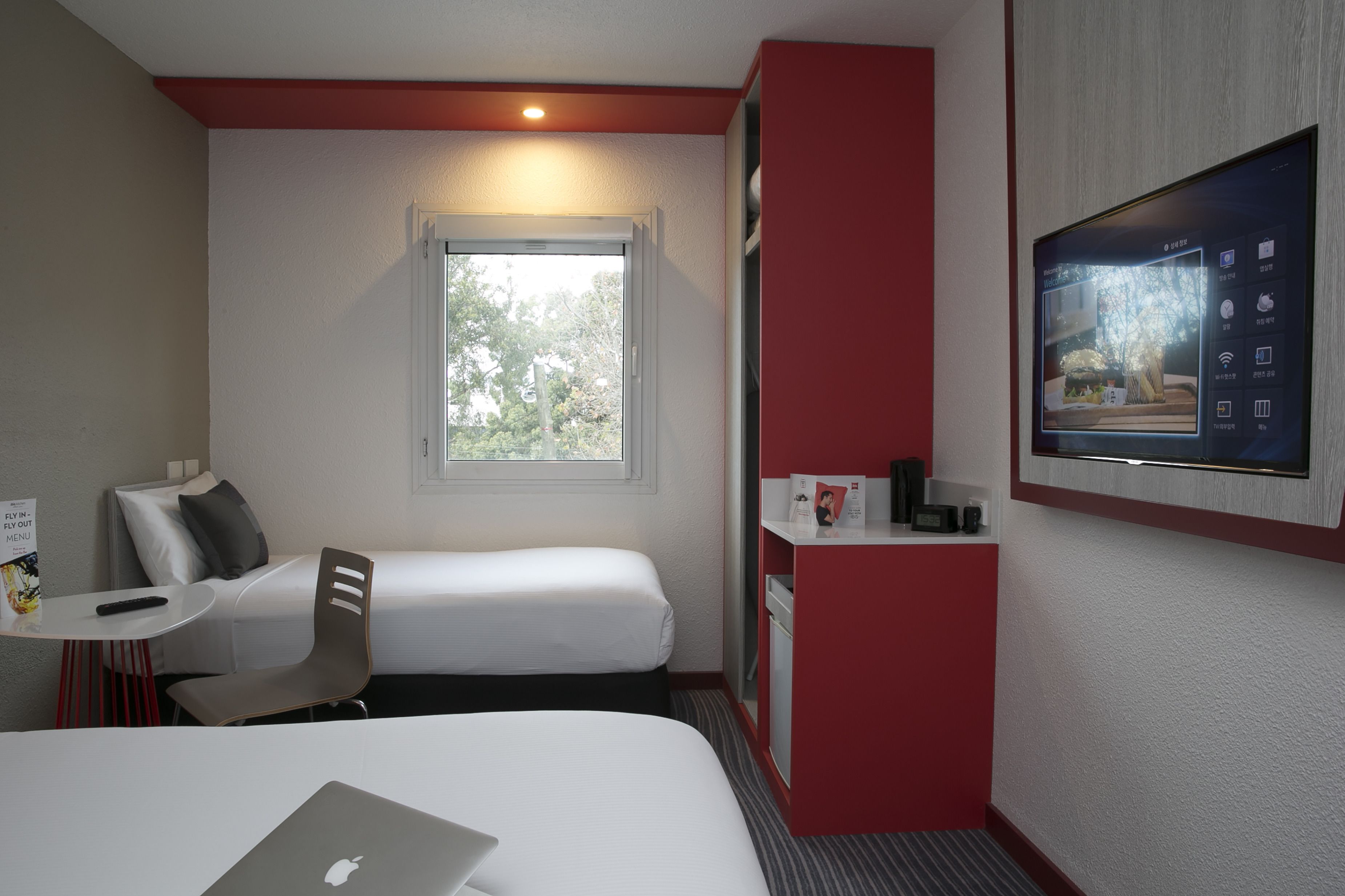Ett hotellrum med två sängar, ett skrivbord med en bärbar dator, en tv som är monterad på väggen och ett fönster med utsikt över träd.