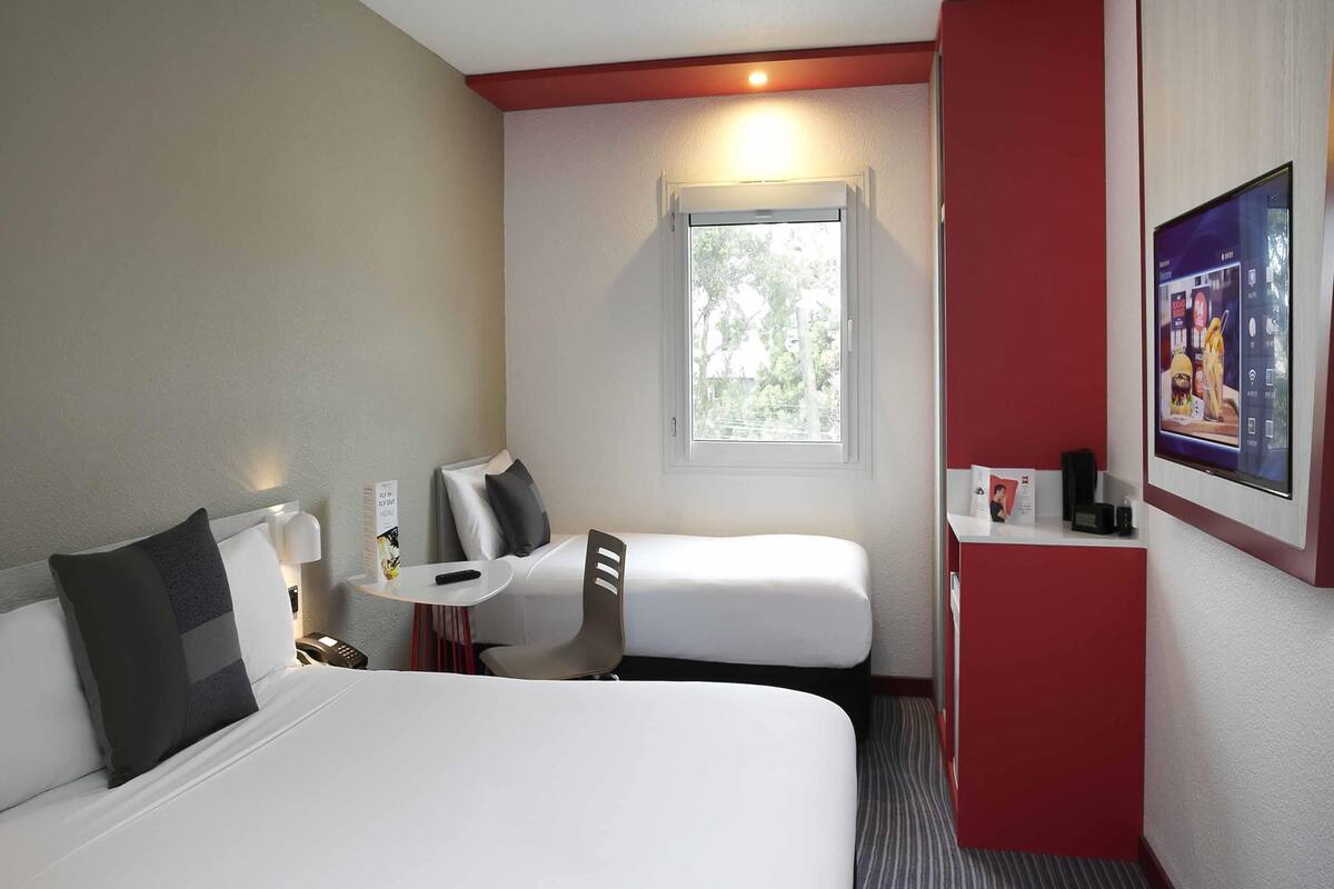 Une chambre d’hôtel avec un lit, un bureau, une chaise, une petite table, une fenêtre et un téléviseur.