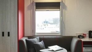 Una habitación moderna con sofá, una mesita, una ventana con vistas a edificios y una puerta.