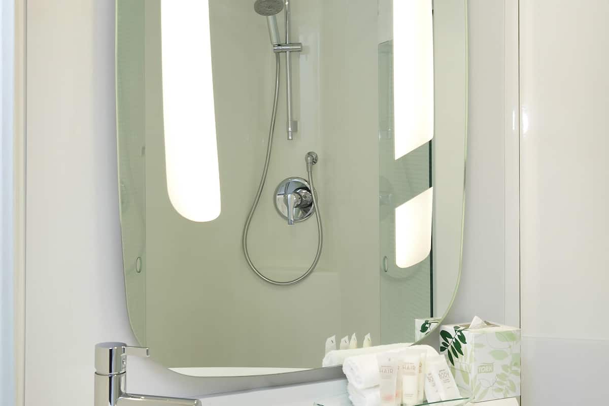 A bathroom with a glass shower enclosure, a white sink, and toiletries on the counter.