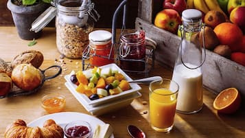 A breakfast table with bread, fruit, cheese, and drinks.