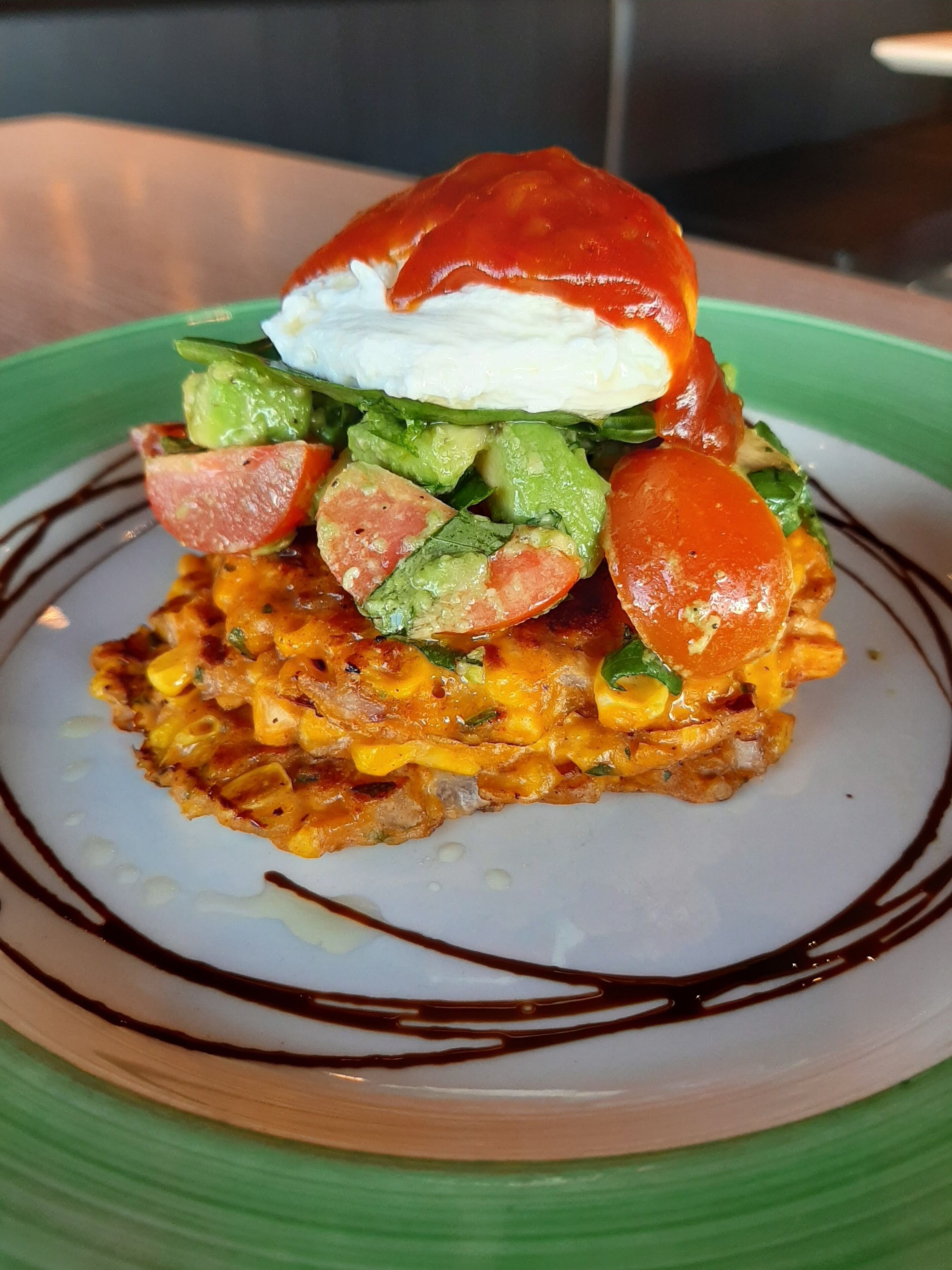 A plate with a food item topped with a poached egg, avocado slices, and a slice of tomato.