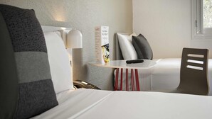 Habitación de hotel con cama, una mesita con un control remoto, una silla y una lámpara en la pared.