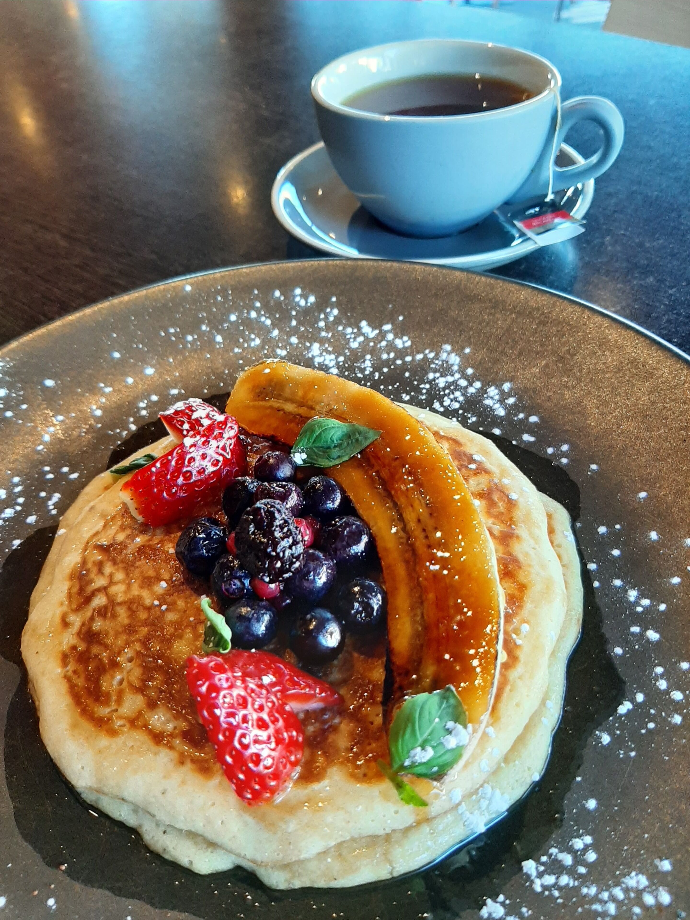 A plate of pancakes topped with berries and syrup, accompanied by a cup of coffee on a saucer.