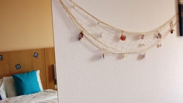 Un letto con biancheria bianca e un cuscino blu, una testiera in legno e una ghirlanda di fiori secchi appesa al muro.