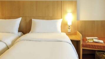 Hotelkamer met twee bedden, een nachtkastje met lamp en een klein tafeltje met telefoon en tas.