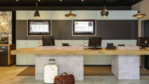 A reception desk with two monitors, a wooden counter, and a concrete base. - ibis Luebeck (Lübeck)