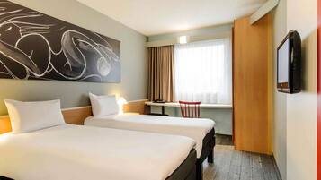 Ein Hotelzimmer mit zwei Betten, einem Schreibtisch, einem Sessel, einem Fernseher und einem großen, abstrakten Gemälde an der Wand.