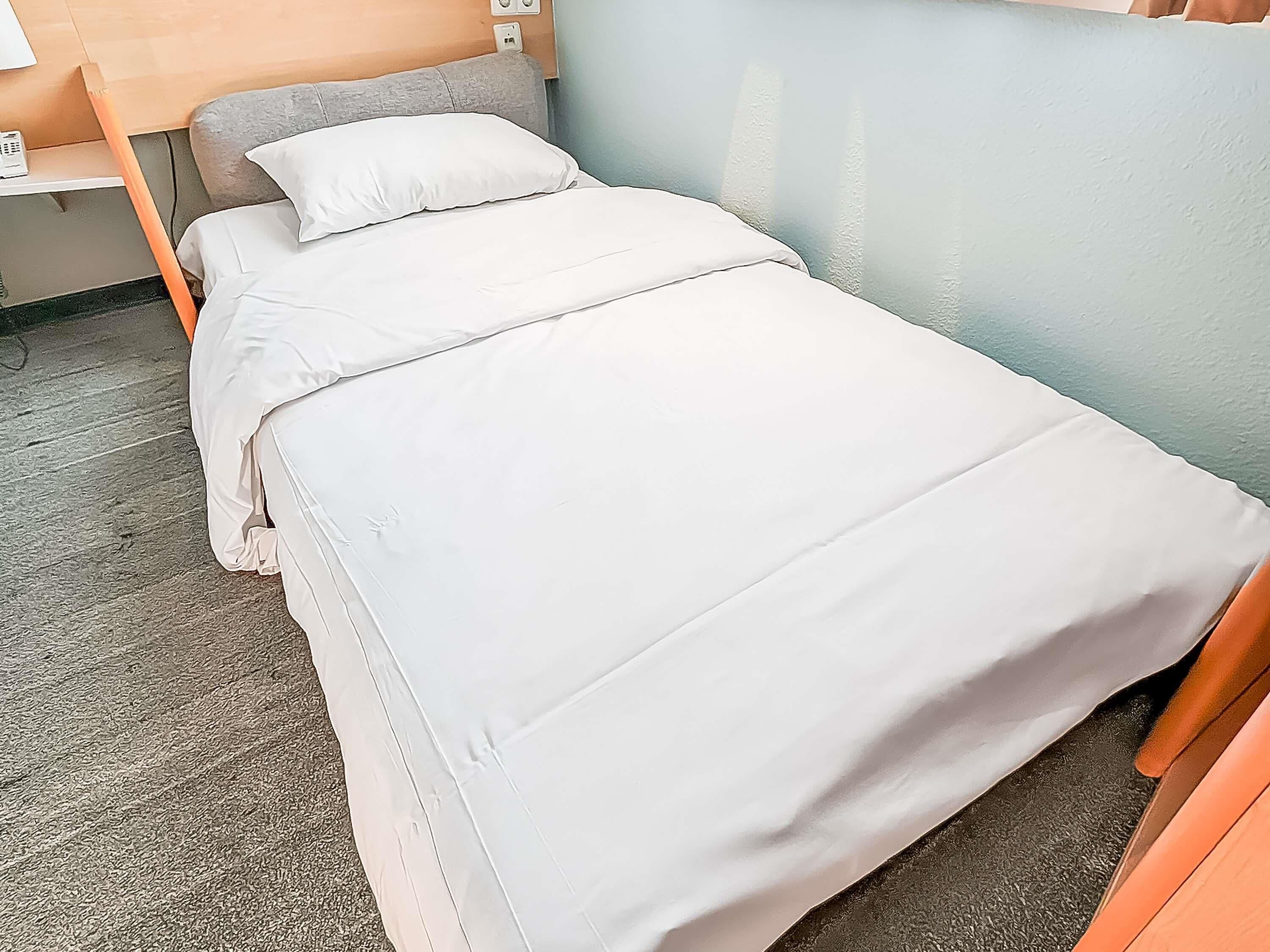A neatly made bed with white linens in a room with a light blue wall and a wooden headboard.
