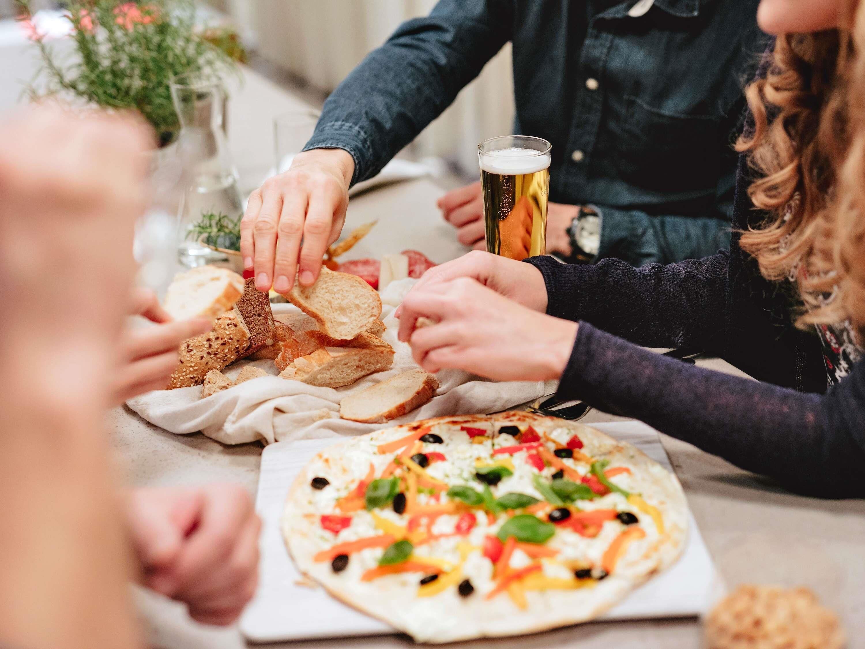 Taula de menjador amb una pizza, pa i un got de cervesa.