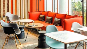 A modern interior with a red sofa, black and white chairs, a round table, and a tall floor lamp. - ibis Luebeck (Lübeck)