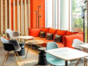 A modern interior with a red sofa, black and white chairs, a round table, and a tall floor lamp. - ibis Luebeck (Lübeck)