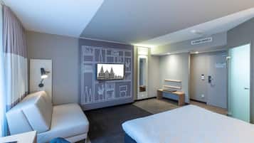 Una habitación de hotel moderna con una cama grande, una zona de estar, un televisor y un escritorio con una computadora portátil.