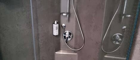 A modern shower enclosure with a handheld showerhead, a handheld soap dispenser, and a clear glass door.