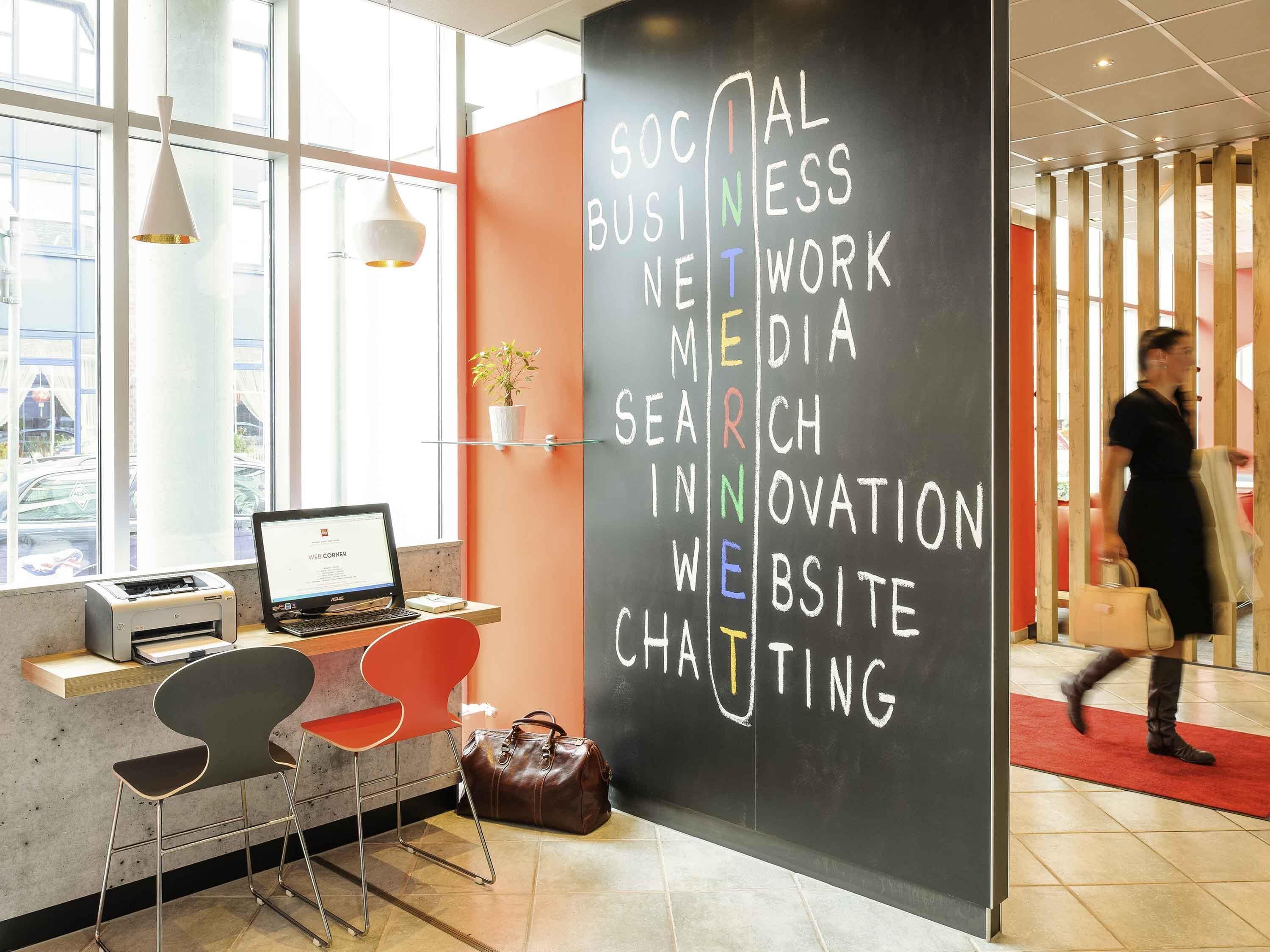 Espaço de trabalho moderno com laptop, impressora e cadeiras vermelhas. Um quadro negro lista tópicos como 'Social Business' e 'Website'.