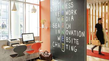 Espaço de trabalho moderno com laptop, impressora e cadeiras vermelhas. Um quadro negro lista tópicos como 'Social Business' e 'Website'.