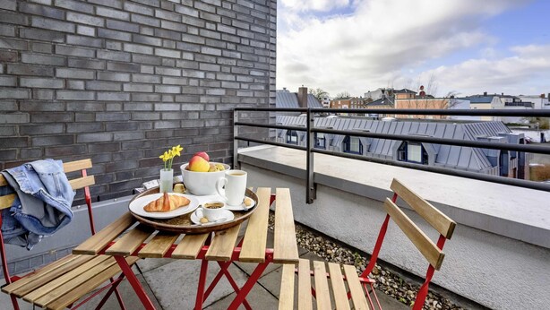 A balcony with a table set for breakfast, including croissants, fruit, coffee, and a vase with flowers. - ibis Luebeck (Lübeck)