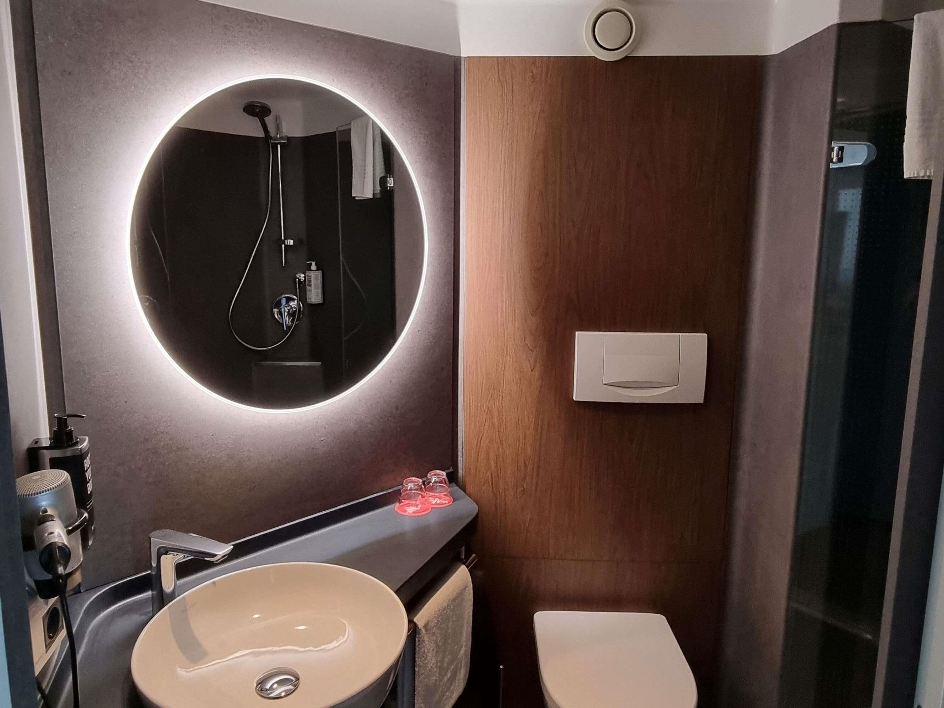 Ein modernes Badezimmer mit rundem Spiegel, Waschbecken, Toilette und Dusche.