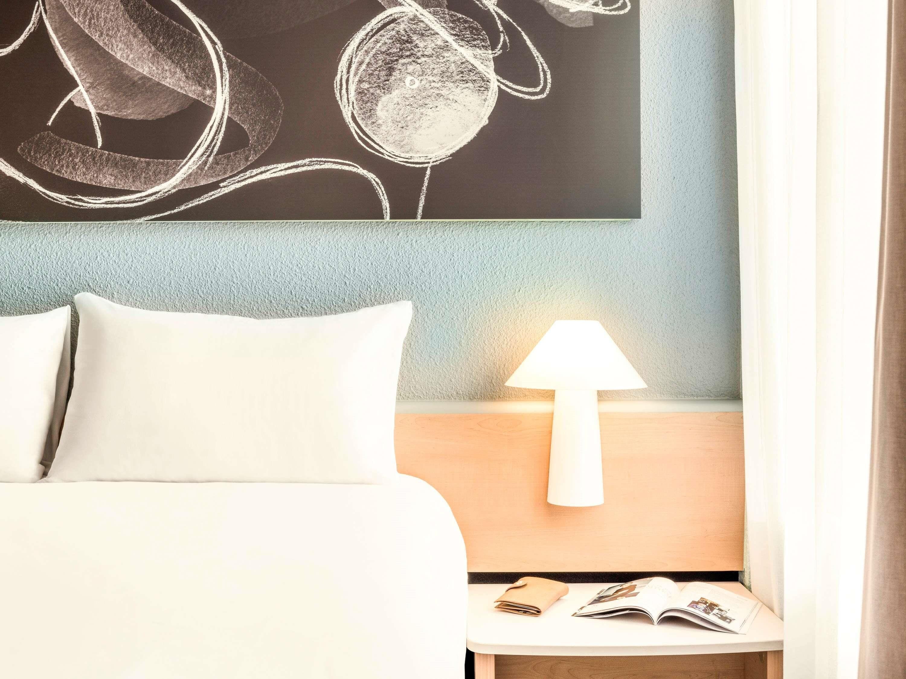 A hotel room with a bed, a nightstand with a lamp, and a wall art piece.