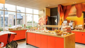 A bright, modern breakfast area with a central island stocked with fruits, cereals, and beverages. - ibis Luebeck (Lübeck)