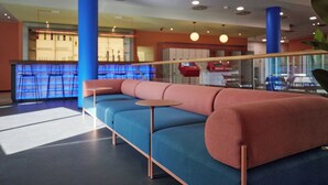 Egy modern, kényelmes pihenősarok, melyben kék és rózsaszín színű kanapé, egy kis, kerek asztal található, a háttérben pedig egy bár is látható.