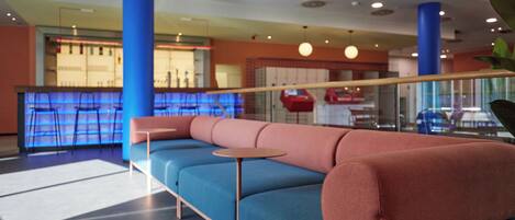 A modern lounge area with a blue and pink sofa, a small round table, and a bar area in the background.