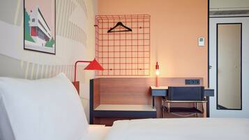 Una habitación de hotel con cama, mesita de noche, lámpara y perchero en la pared.
