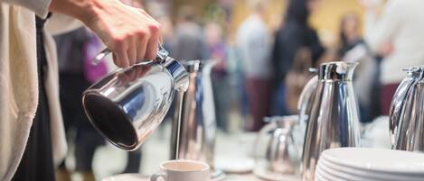 Una persona sirve café en una taza sobre una mesa con platos apilados y varias cafeteras.
