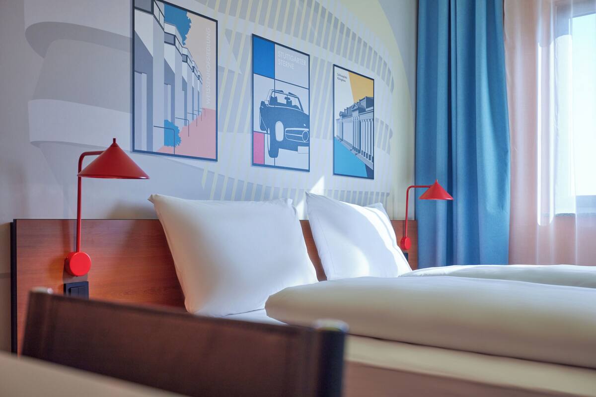 A hotel room with a wooden headboard, white bedding, and two red lamps.
