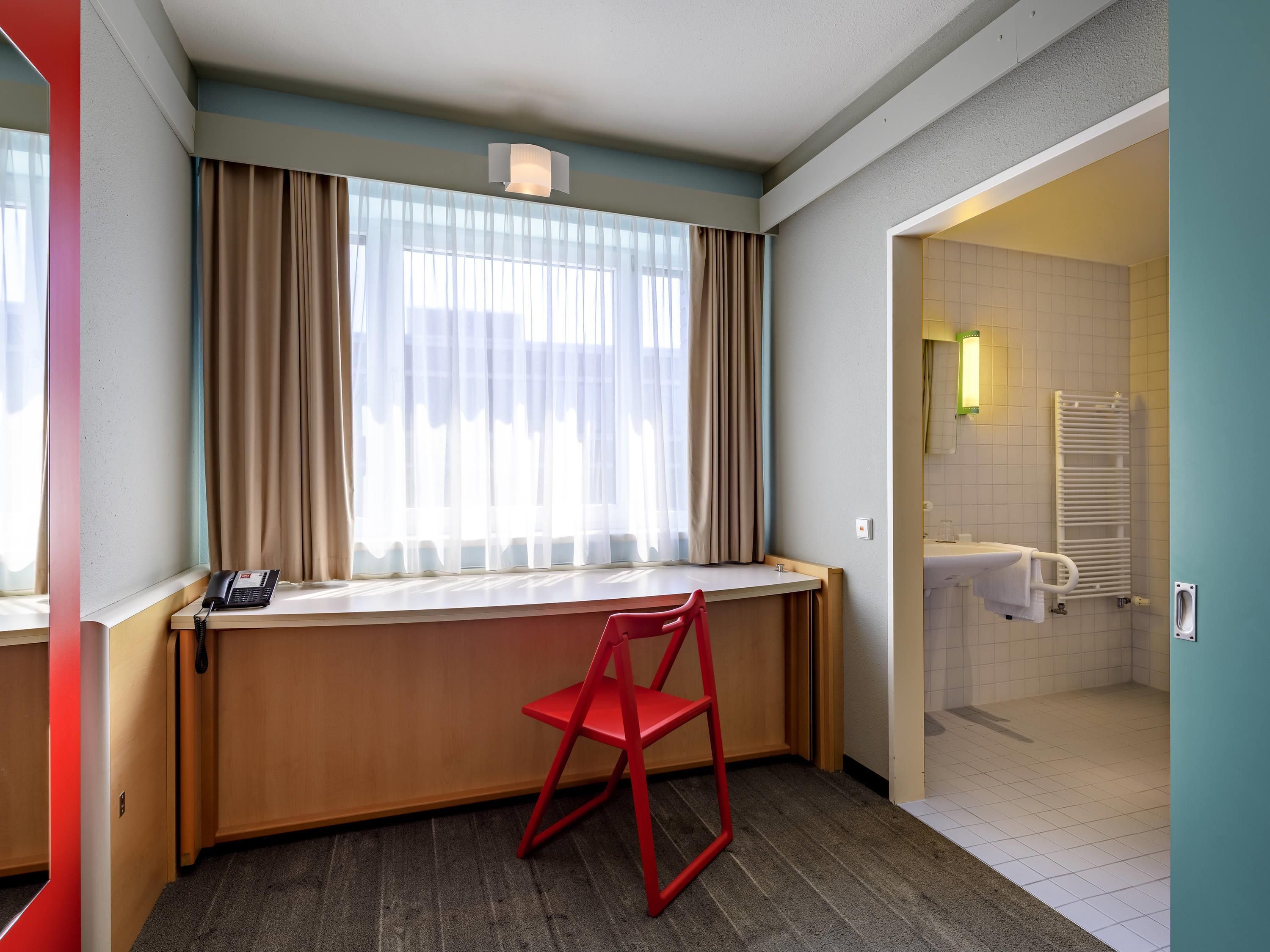 Ein Hotelzimmer mit Schreibtisch, Stuhl und Blick ins Bad.