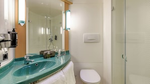 A modern bathroom with a glass shower enclosure, a sink with a towel, and toiletries. - ibis Hamburg Alsterring (Hamburg)