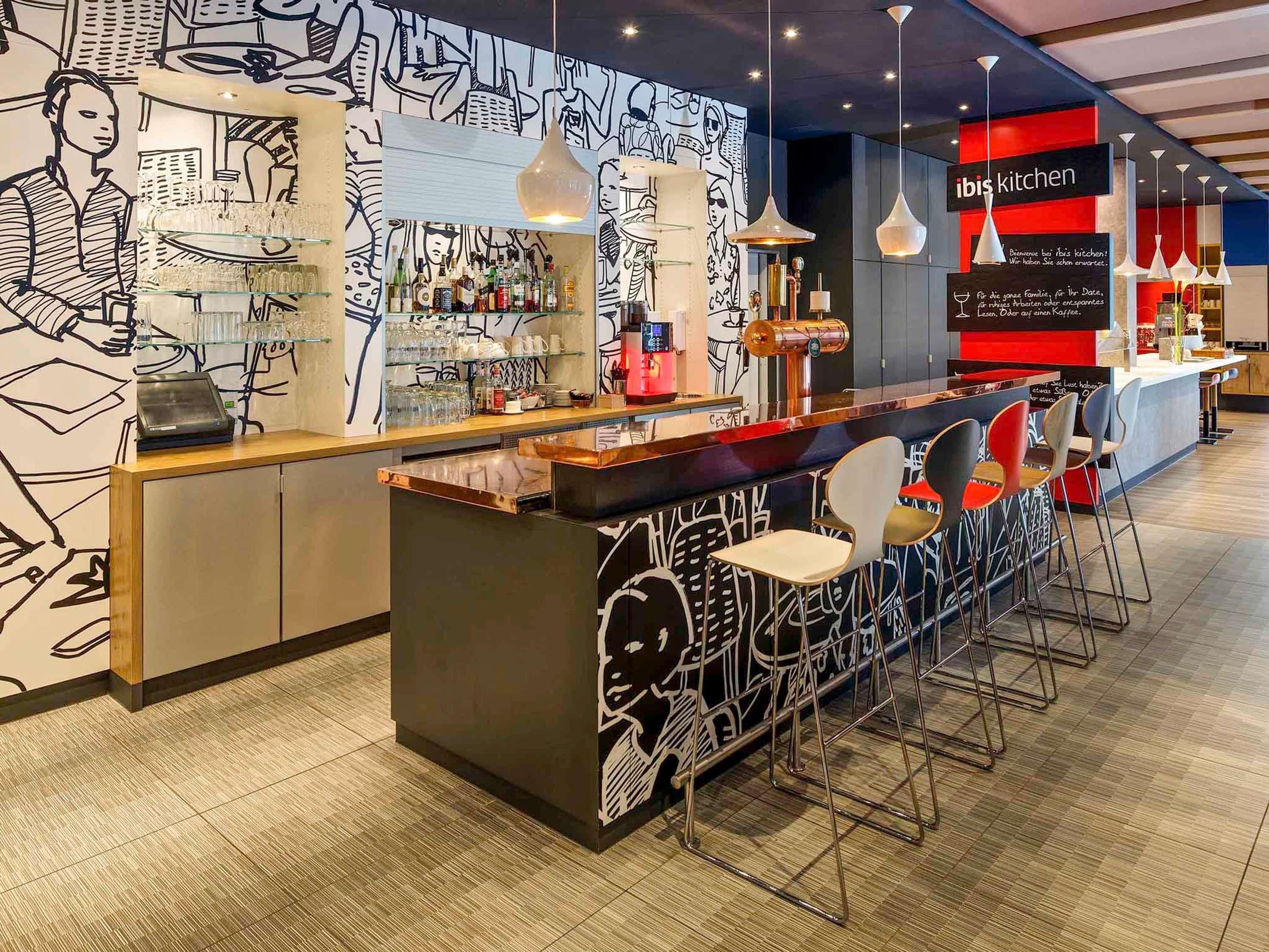 A modern bar area with a counter, stools, and a wall with abstract art.