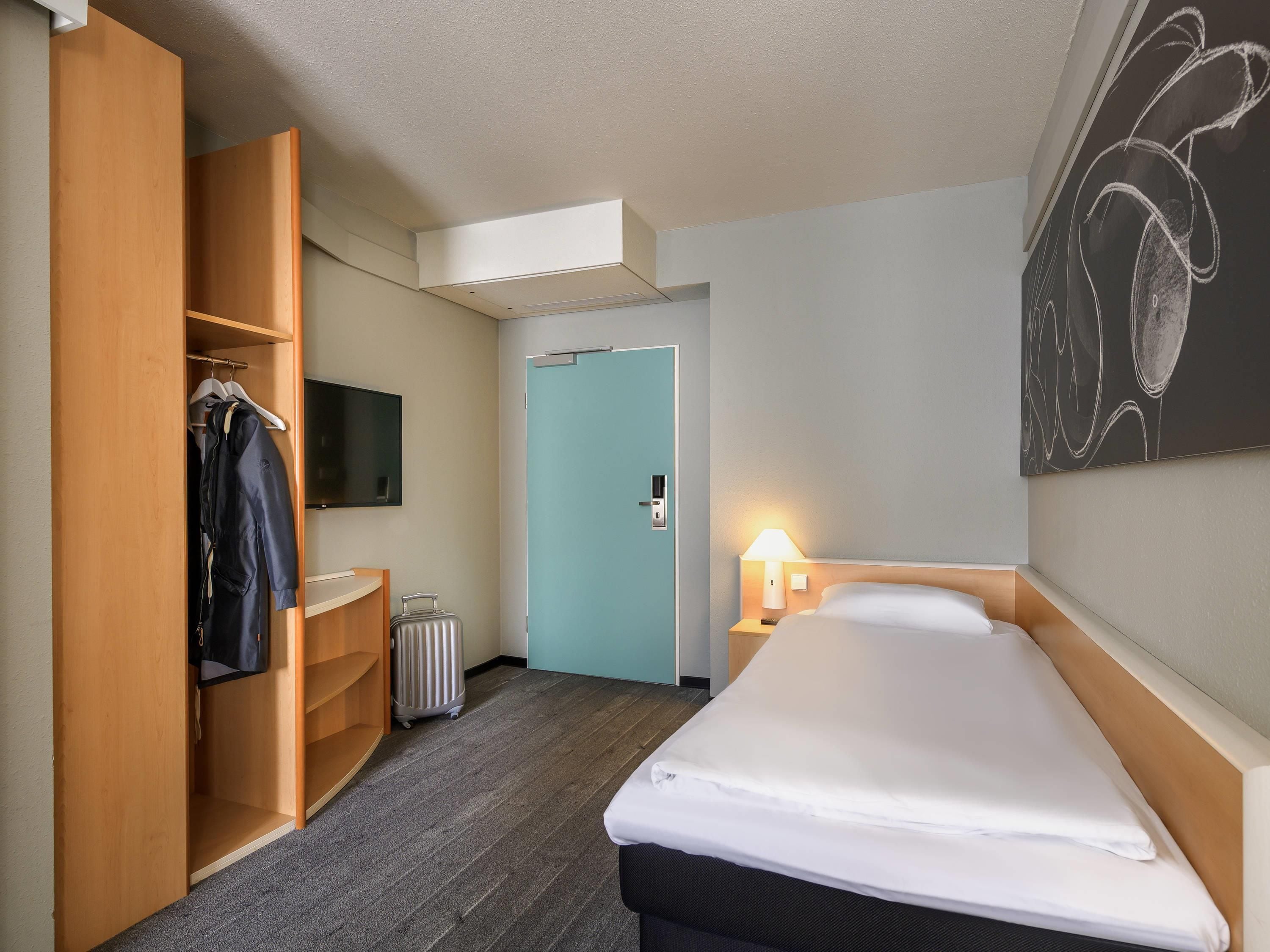 Une chambre d’hôtel comprenant un lit, une armoire, un téléviseur, une porte et une œuvre d’art accrochée au mur.