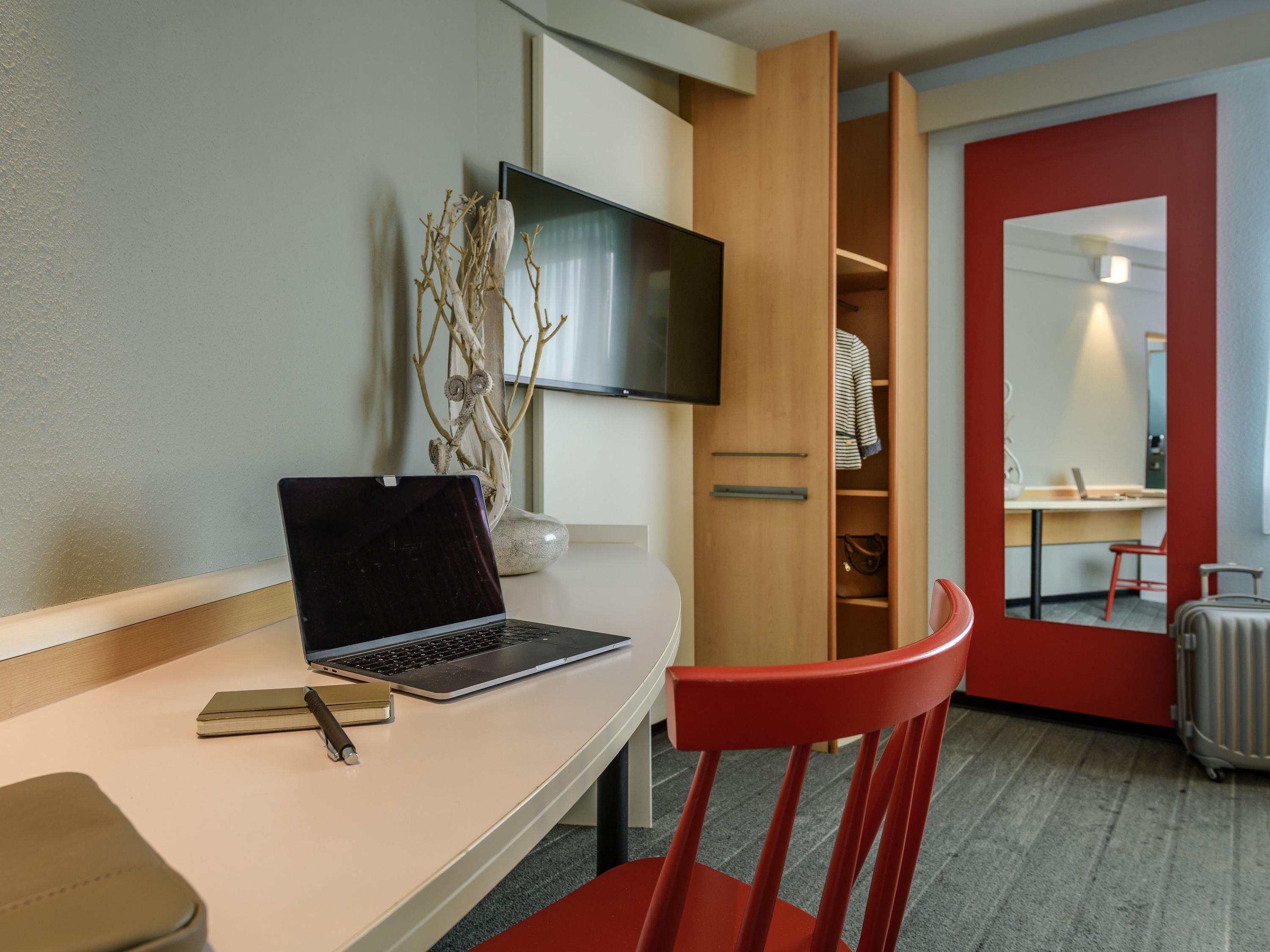 Habitación de hotel con escritorio, laptop, silla y armario con espejo.