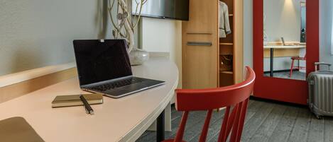 Habitación de hotel con escritorio, laptop, silla y armario con espejo.