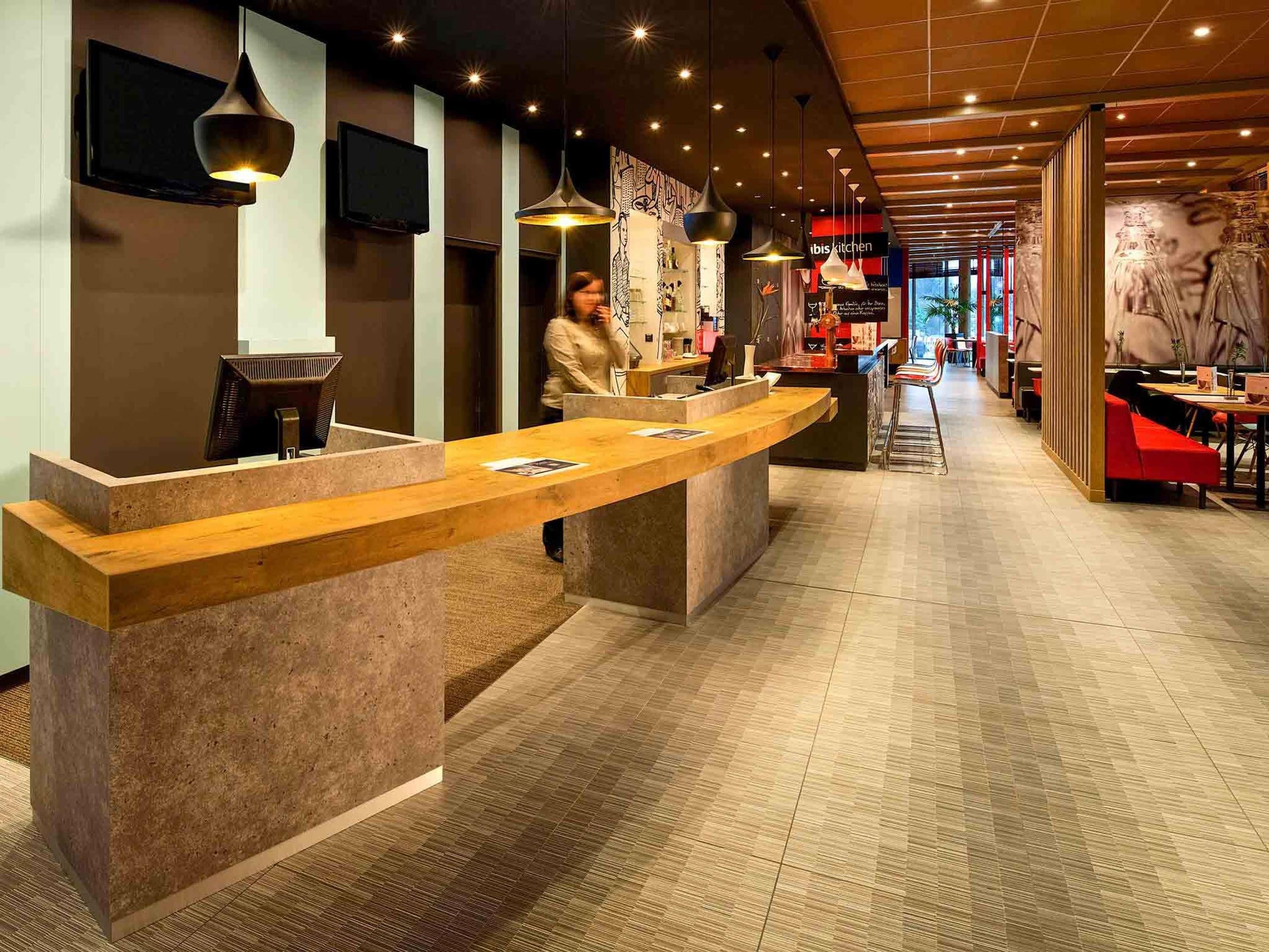 Ein moderner Hotel-Empfangsbereich mit einer gebogenen Rezeption, einem an der Wand montierten Fernseher und einer Person hinter dem Empfängertresen.