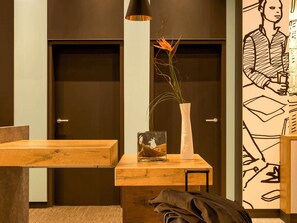 Habitación de hotel con un escritorio de madera, un florero con una planta y una pared con un mural en blanco y negro.