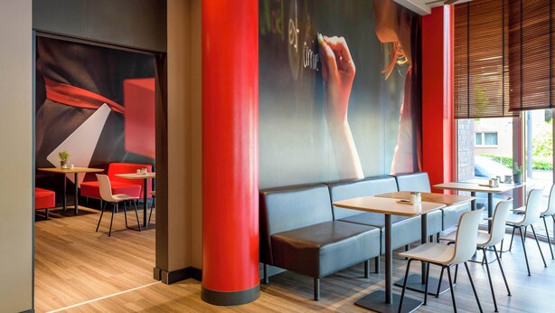 Ein modernes Restaurant mit Holzboden, roten und grauen Sitzmöbeln und einer großen Wandmalerei.