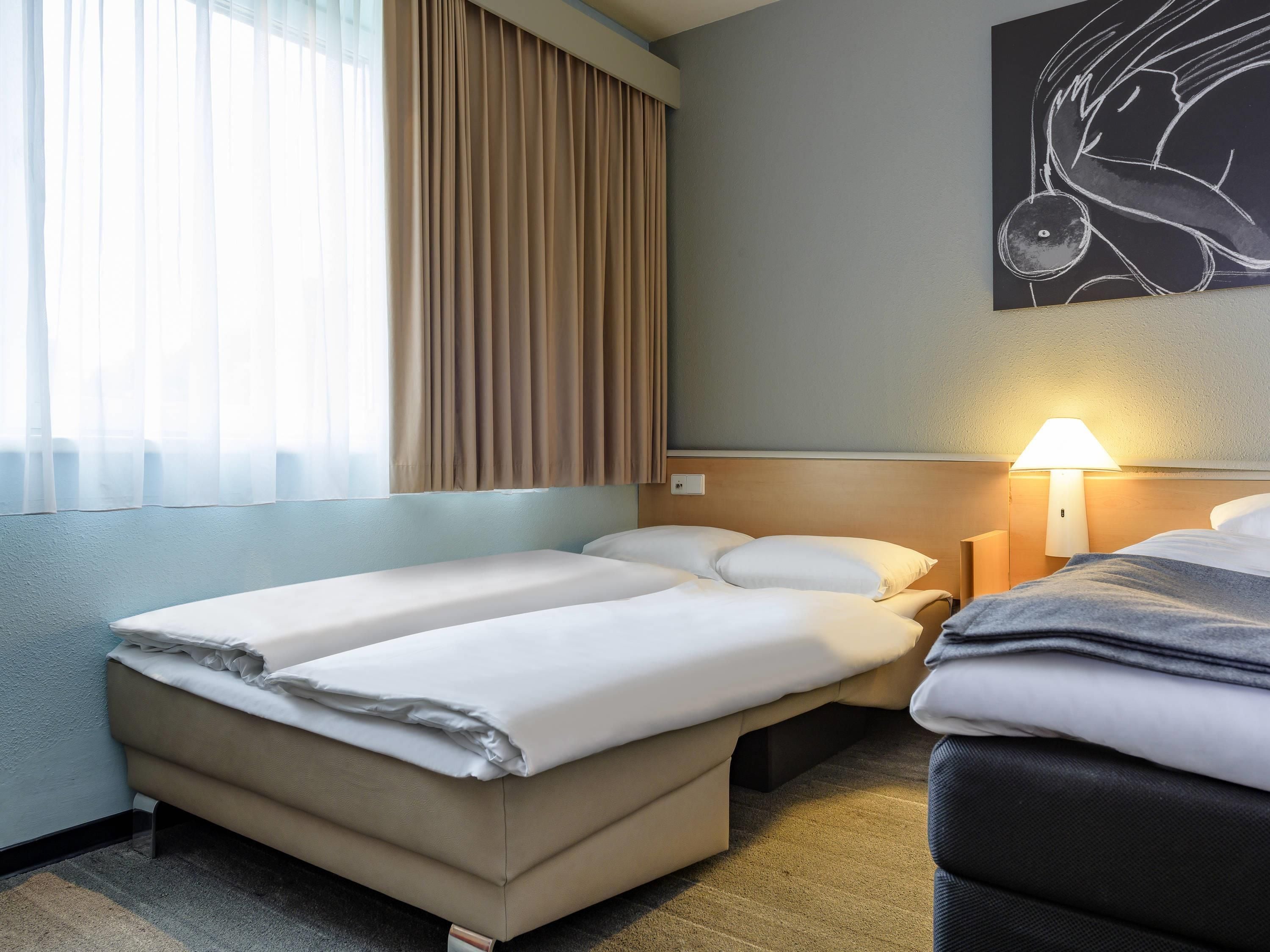 A hotel room with two beds, a bedside lamp, and a painting on the wall.