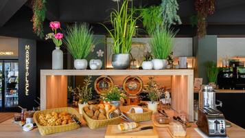 Un comptoir de boulangerie où sont exposés divers produits de boulangerie, une machine à café et des plantes décoratives.
