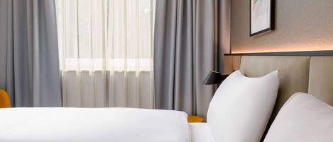 A hotel room with a bed, a nightstand, a lamp, and a window with curtains.