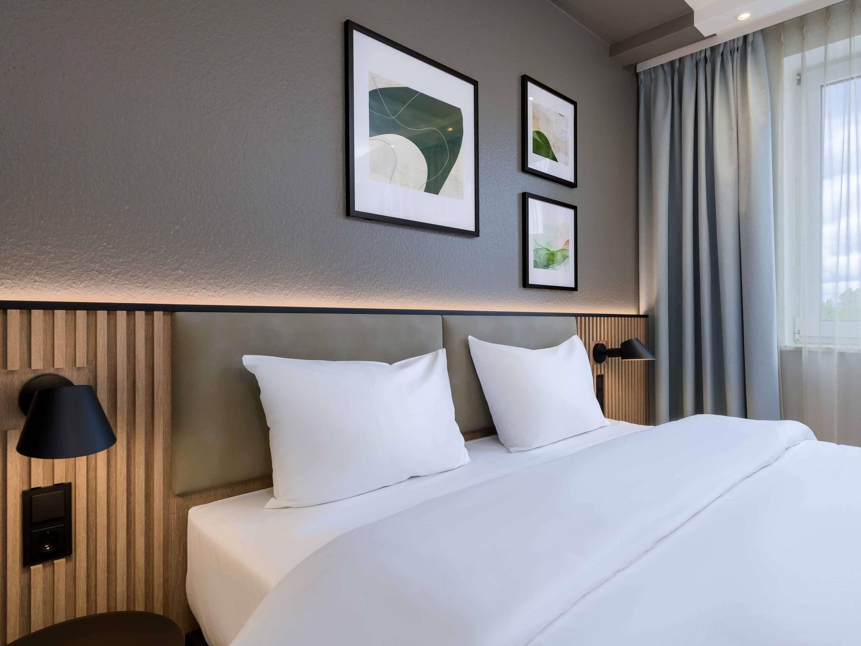 Ein Hotelzimmer mit einem großen Bett, zwei Kissen, einem Kopfteil, einer Nachttischlampe und drei gerahmten Bildern an der Wand.