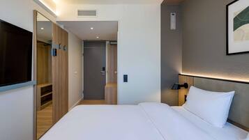 A hotel room with a bed, a TV, a wardrobe, and a wall-mounted lamp.