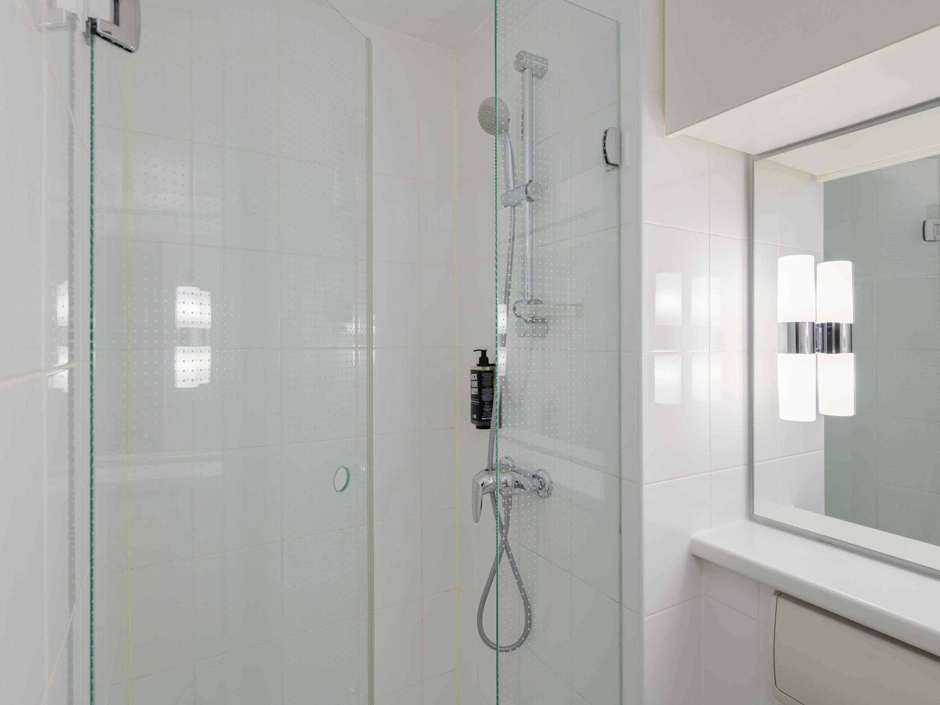 Ein modernes Badezimmer mit einer einteiligen Glasdusche, einem wandmontierten Spiegel und einer weißen Fliesenwand.