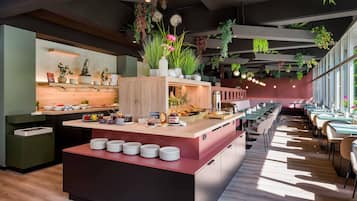 Ein modernes Restaurant mit einer zentralen Insellounge, Esstischen und hängenden Pflanzen.