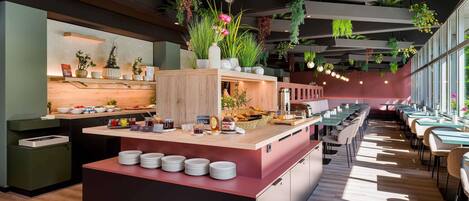 Un interior de restaurante moderno con una isla central, mesas para comer y plantas colgantes.